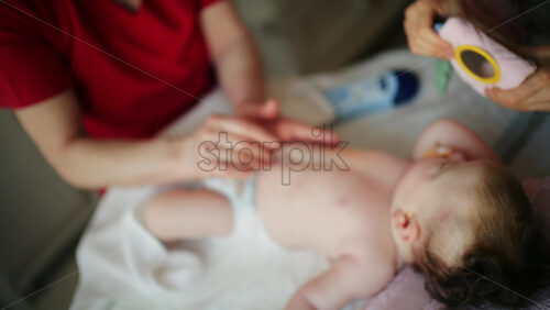Infant lying on back while an adult gently rubs lotion or oil onto the baby's body