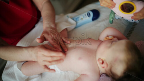 Infant lying on back while an adult gently rubs lotion or oil onto the baby's body