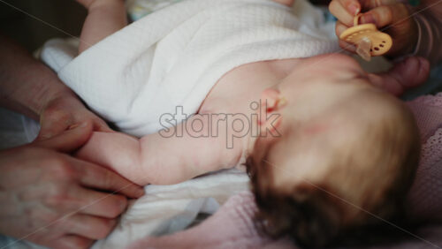 Close up of caregiver softly massaging a baby's arms and upper chest area while the infant rests calmly