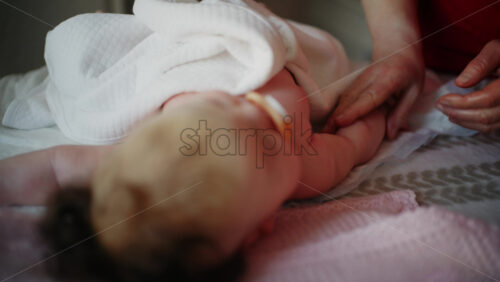 Baby lying on their back while an adult massages them and the mother holds the pacifier in the baby's mouth