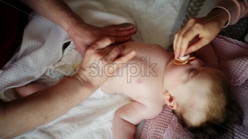 Baby lying on their back while an adult massages them and the mother holds the pacifier in the baby's mouth