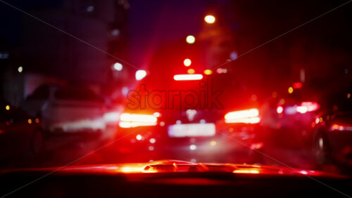 View from inside a vehicle looking ahead at traffic with red brake lights glowing at night