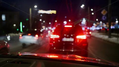 Night city traffic with multiple vehicles ahead, brake lights glowing red and streetlights lining the road