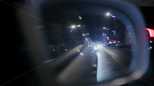 Close up of a side mirror at night with bright headlights from a car behind creating lens flare