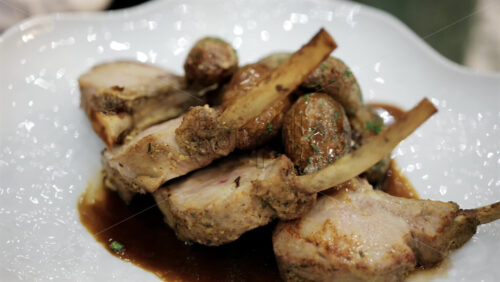 Rack of lamb served with roasted potatoes and sauce on a white plate
