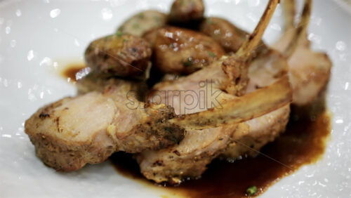 Rack of lamb served with roasted potatoes and sauce on a white plate