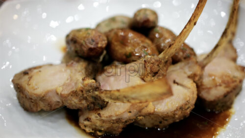Rack of lamb served with roasted potatoes and sauce on a white plate