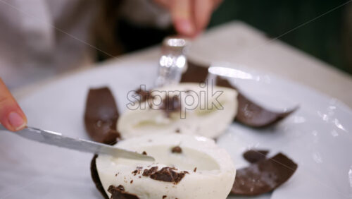 Close up of a coconut shaped dessert with a chocolate shell being cut open to reveal a creamy interior
