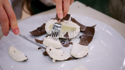 Close up of a dessert shaped like a coconut being opened with a fork, revealing a creamy white interior