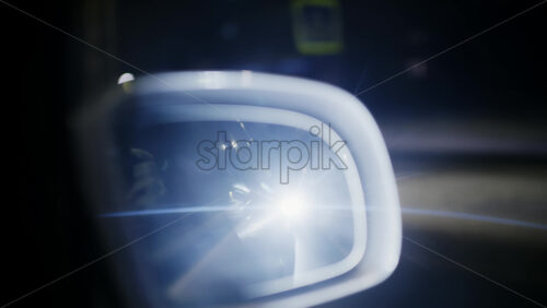 Side mirror reflecting bright headlights from a vehicle behind at night