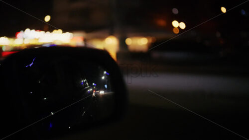 Car side mirror reflecting passing city lights while driving at night