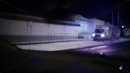 Ambulance with flashing blue lights driving along a snowy residential street at night