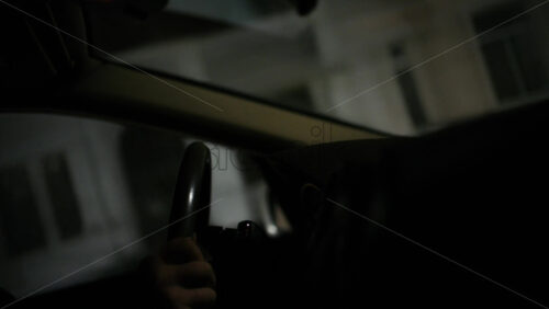 Close up of a driver's hand holding a steering wheel inside a car at night