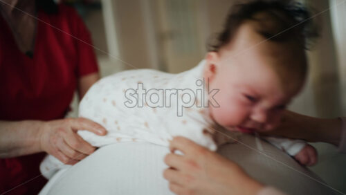 Baby placed on tummy on a stability ball while adults support the infant's torso and shoulders