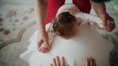 Baby placed on tummy on a stability ball while adults support the infant's torso and shoulders