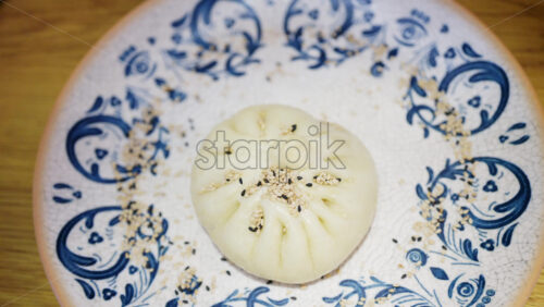 Close up of a steamed bun topped with sesame seeds on a decorative ceramic plate