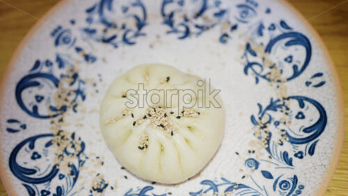 Close up of a steamed bun topped with sesame seeds on a decorative ceramic plate