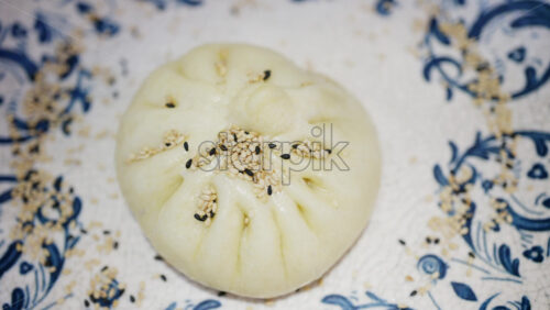 Close up of a steamed bun topped with sesame seeds on a decorative ceramic plate