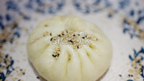 Close up of a steamed bun topped with sesame seeds on a decorative ceramic plate