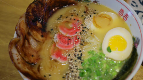Detailed close up of ramen soup with pork slices, egg half, noodles, and chopped green onions