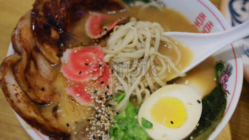 Close up of a spoon picking up ramen showing toppings and steaming broth