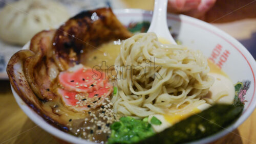 Close up of a spoon picking up ramen showing toppings and steaming broth