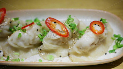 Row of pan fried dumplings topped with sliced red chili and green onions on a ceramic plate