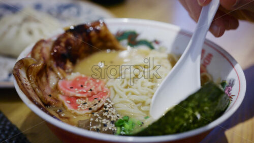 Close up of a spoon picking up ramen showing toppings and steaming broth