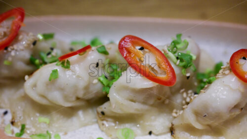 Row of pan fried dumplings topped with sliced red chili and green onions on a ceramic plate