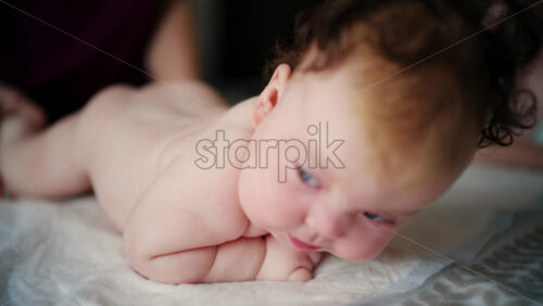 Baby lying on tummy on a soft surface, lifting head and looking downward during tummy time