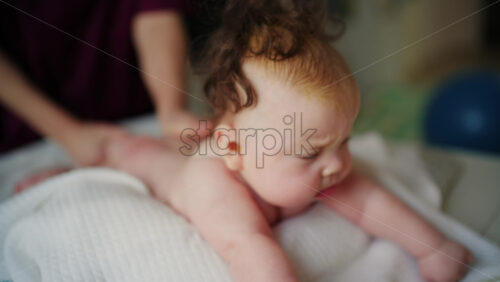 Baby lying on their tummy while an adult massages them and performs mobility exercises