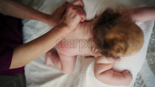 Overhead view of baby during a gentle massage, caregiver's hands supporting the infant's legs