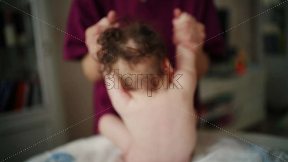 Infant lying on back during a care routine, adult hands softly supporting the baby's limbs