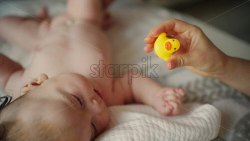 Woman trying to distract a crying baby lying on a blanket during massage with a toy