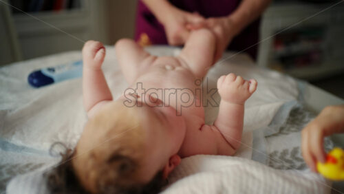 Woman trying to distract a crying baby lying on a blanket during massage with a toy