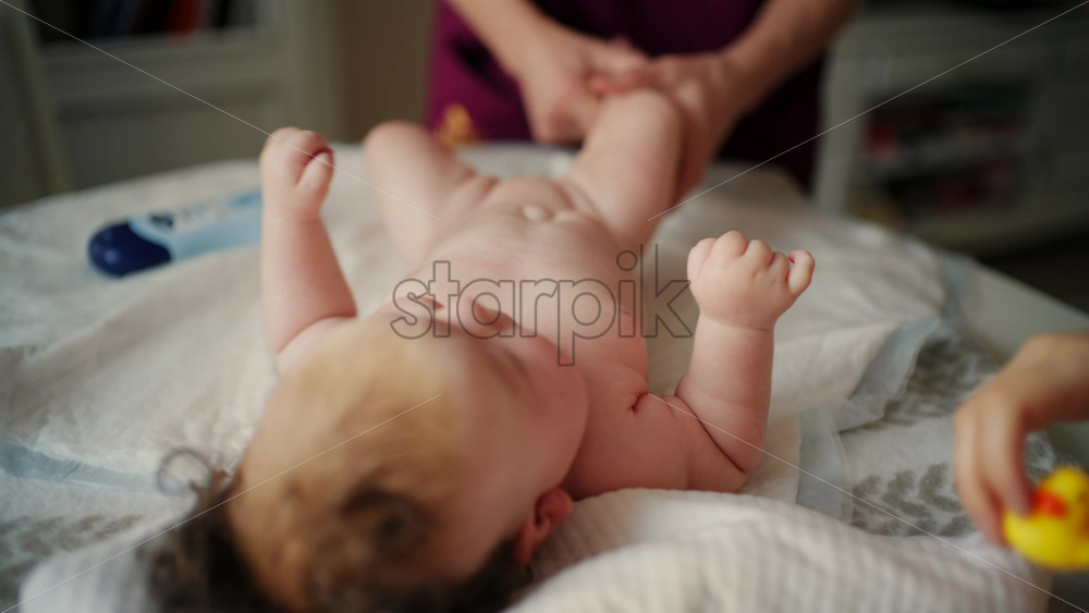Woman trying to distract a crying baby lying on a blanket during massage with a toy