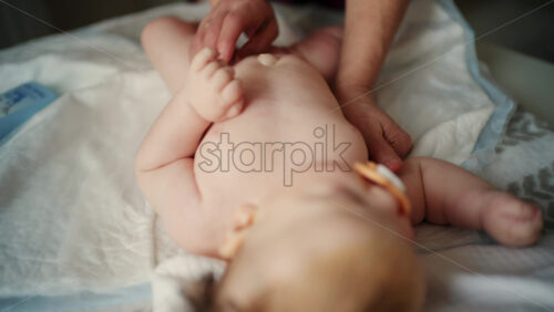 Baby lying on their back while an adult massages them and the mother holds the pacifier in the baby's mouth