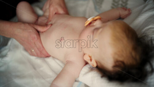 Baby lying on their back while an adult massages them and the mother holds the pacifier in the baby's mouth