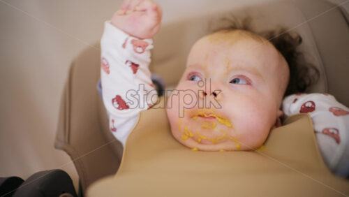 Infant seated in a high chair while an adult feeds the baby with a spoon