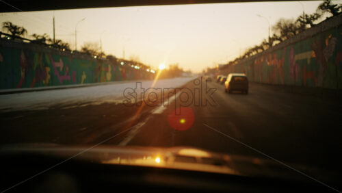 Point of view driving shot on a multi lane road at sunset, with strong sun flare and long shadows