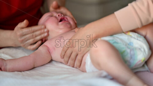 Close up of a baby crying while a caregiver gently massages the face on a soft surface