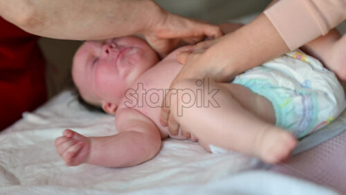 Close up of a baby crying while a caregiver gently massages the face on a soft surface