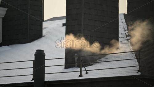 Warm steam rising from a rooftop ventilation outlet on a snow covered building during winter