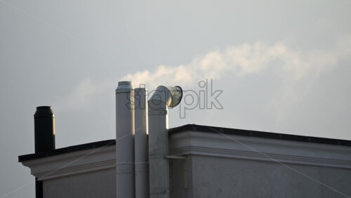 Close up of chimney pipes on a residential building with smoke drifting into the cold sky