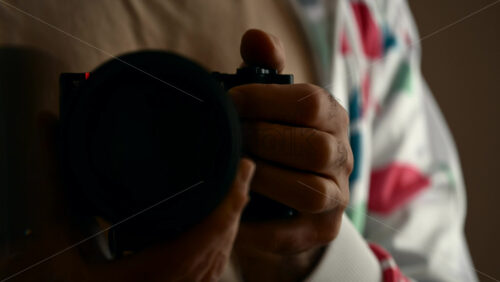 Close up of a man's hands holding a camera with a large lens, preparing to shoot