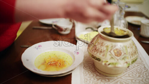 Person stirring hot soup in a decorative ceramic pot on a dining table. Traditional homemade meal being served.