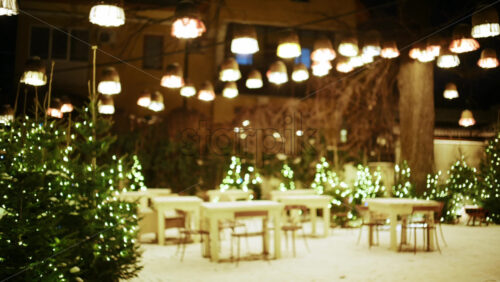 Cozy outdoor cafe decorated with string lights and small illuminated trees in winter