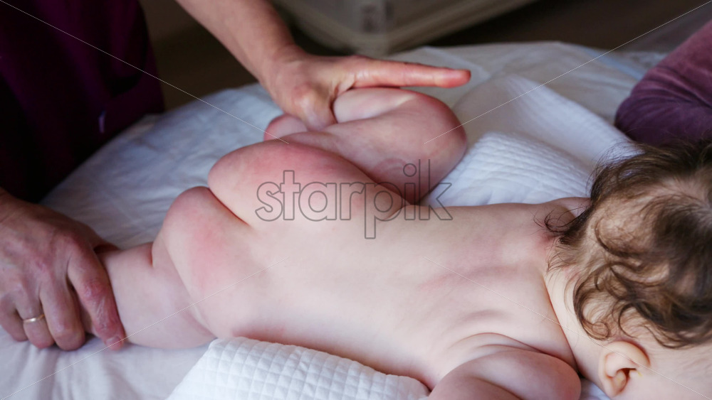 Close up of a caregiver holding a baby's small foot while tending to the infant on a bed
