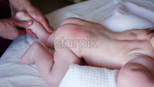 Baby lying on their tummy while an adult massages them and performs mobility exercises