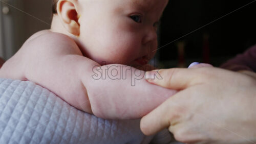 Woman trying to distract a crying baby lying on a blanket during massage with a toy